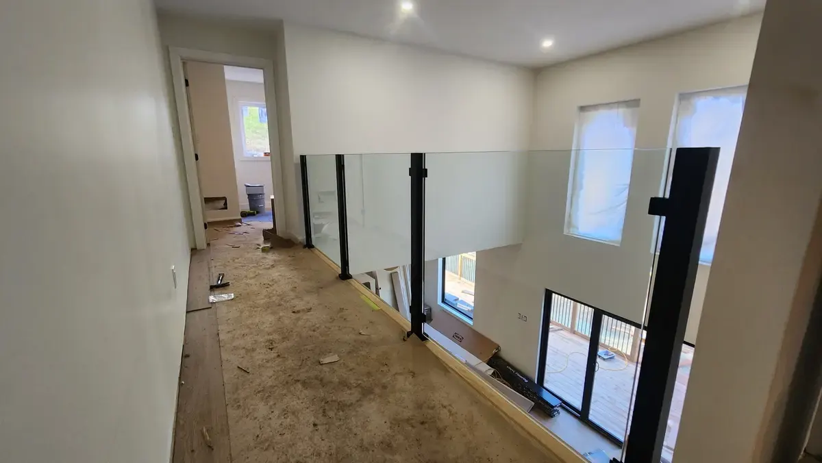 Glass panel loft railing with black steel posts at hallway level in new construction