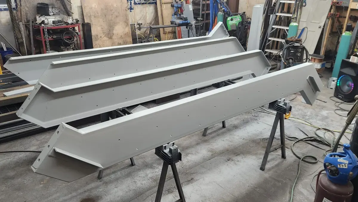 Precision-fabricated painted steel channel brackets on sawhorses in workshop