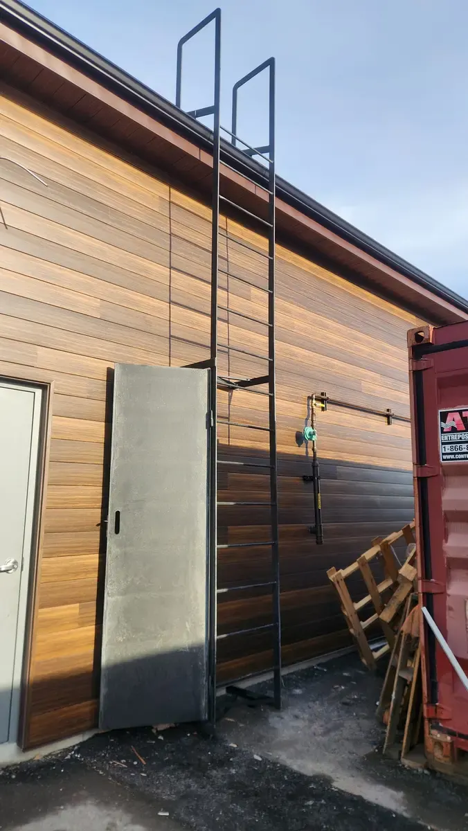 Fixed black steel roof access ladder with top grab rails on a commercial building exterior