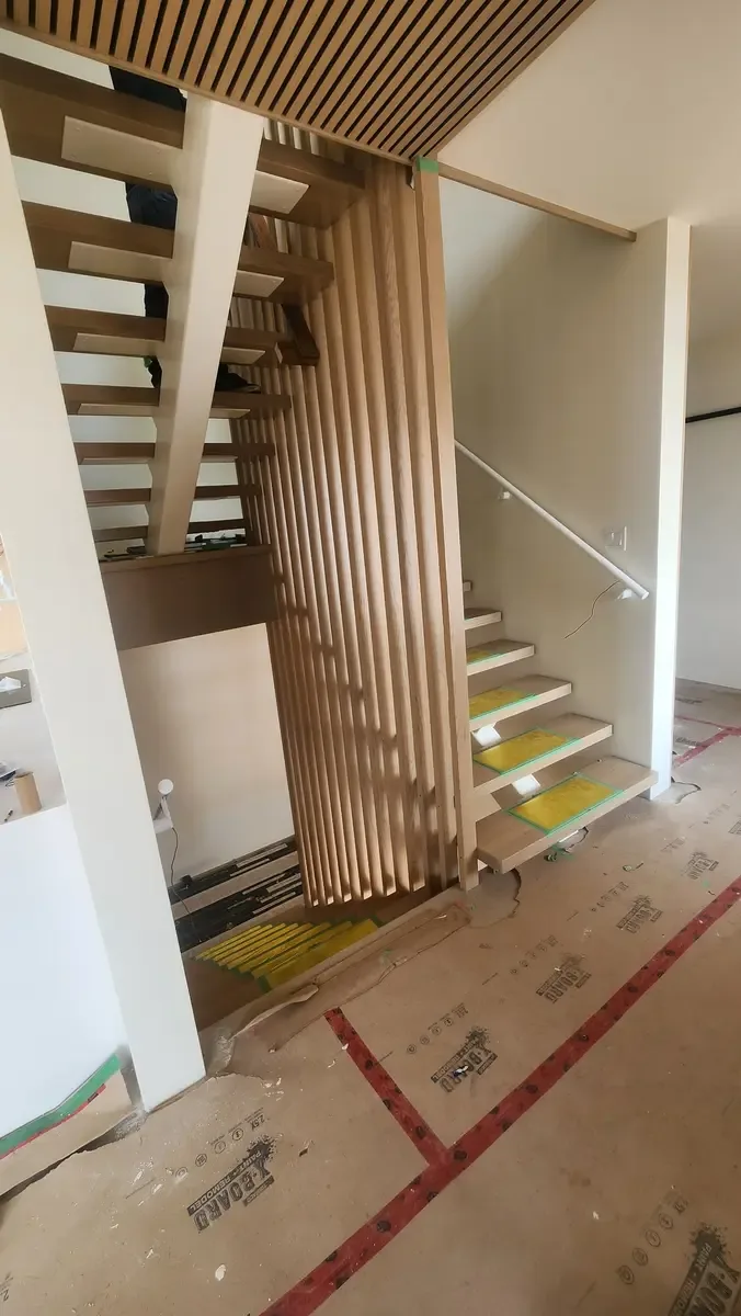 Modern floating staircase with wood slat privacy divider and matching ceiling in new construction