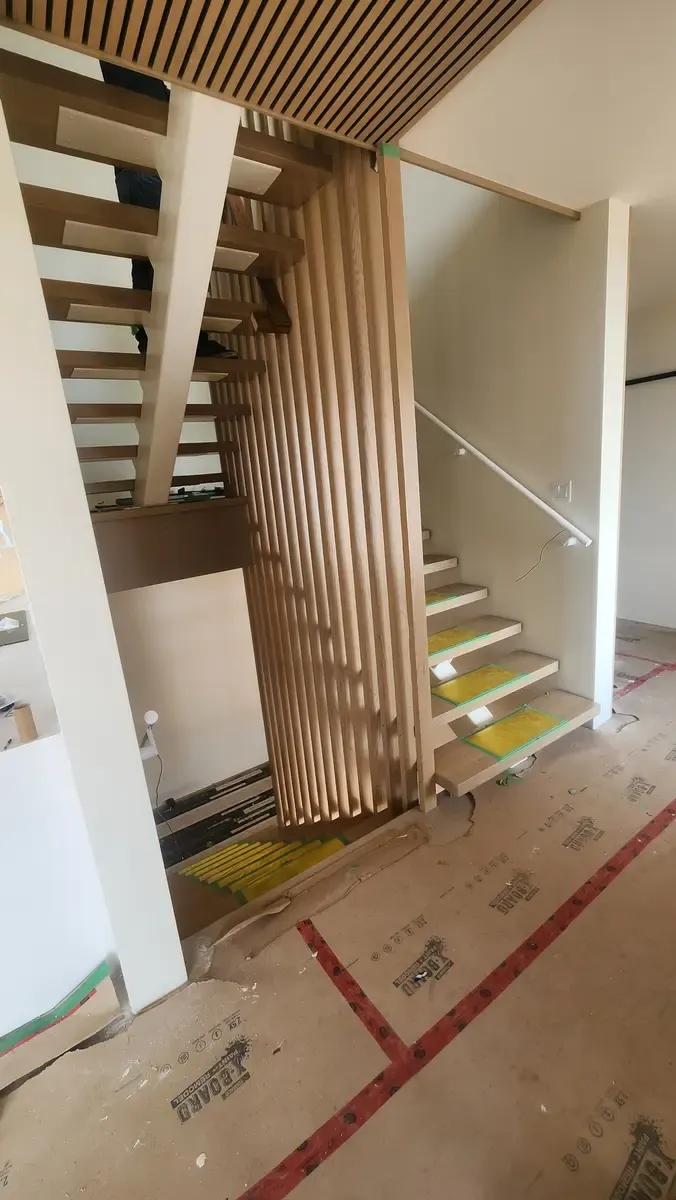 Modern floating staircase with wood slat privacy divider and matching ceiling in new construction
