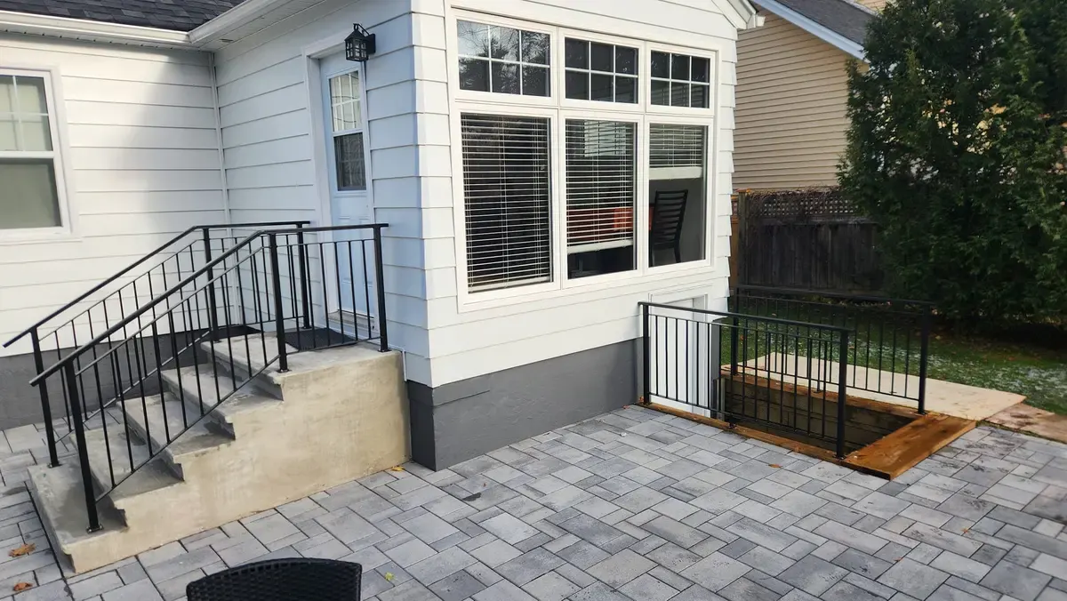 Residential exterior railing on patio with cellar access hatch, black steel with stone pavers