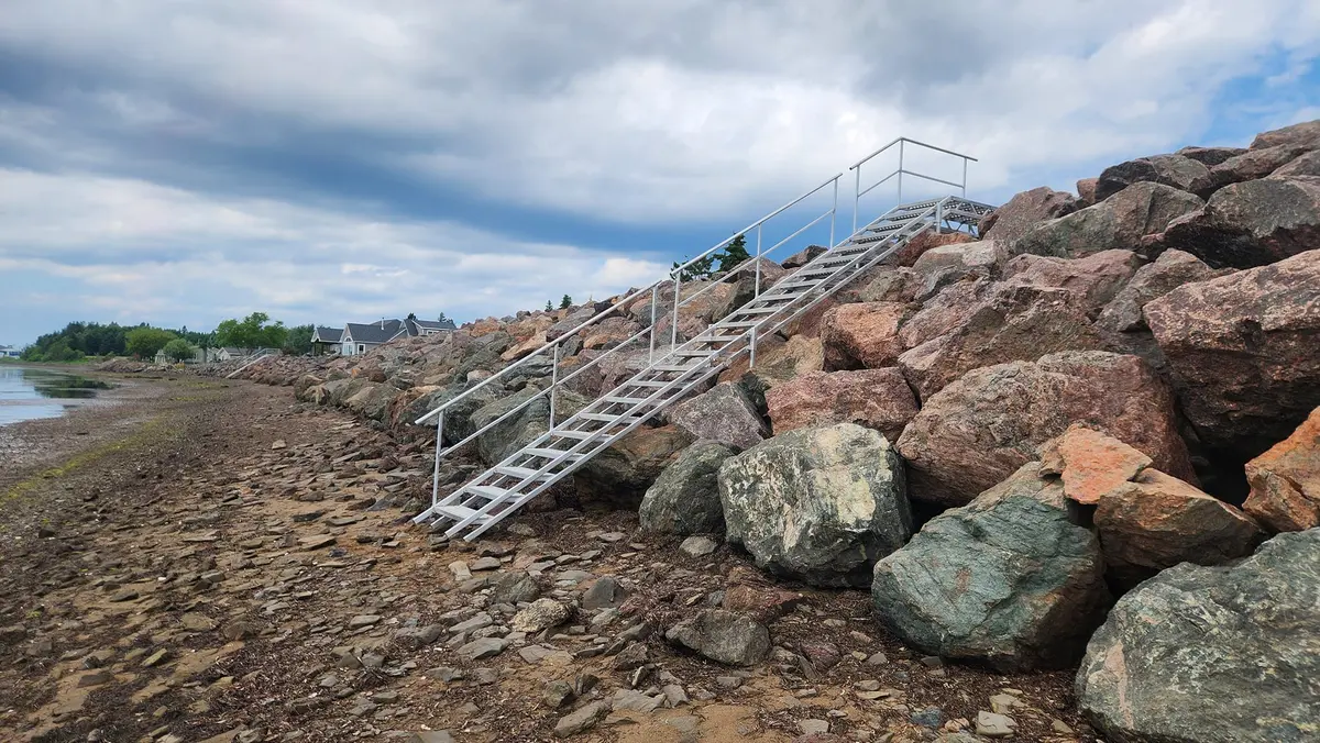 Alternate angle of aluminum beach access stairs on rocks with town visible in background