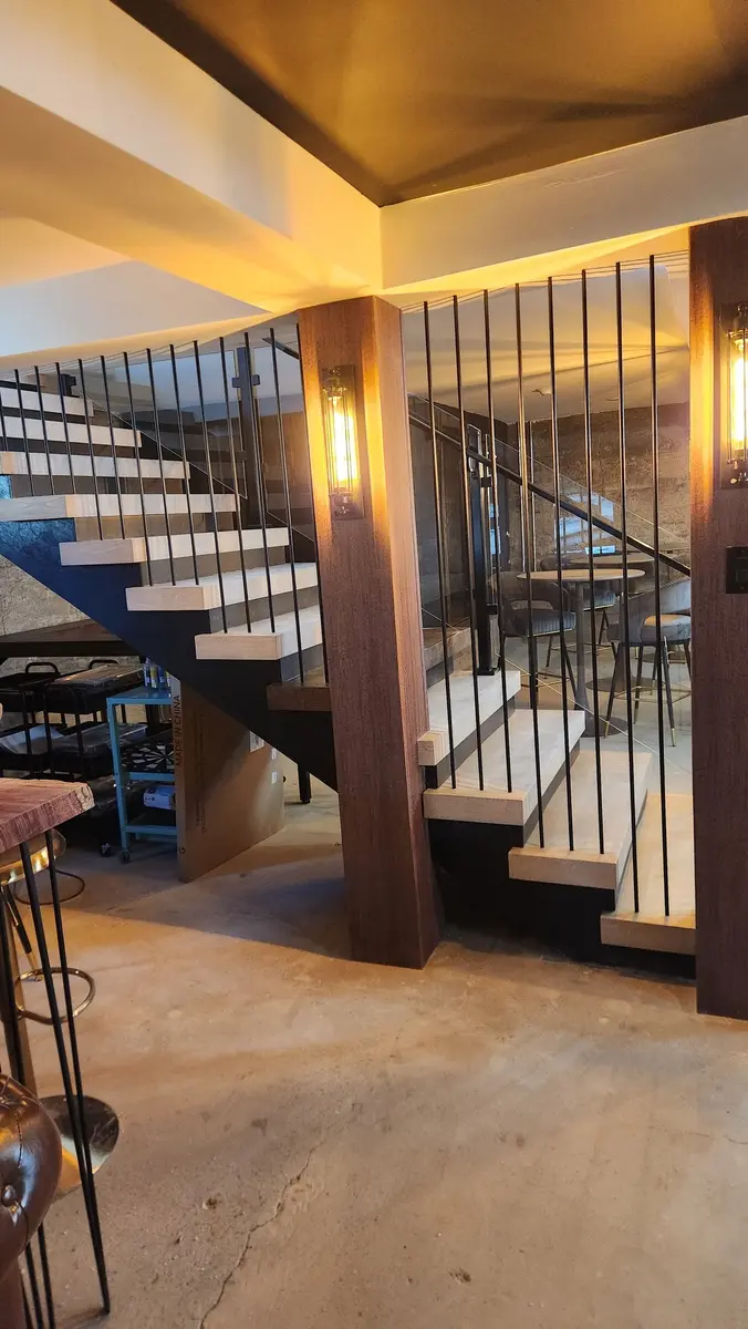 Restaurant staircase with ambient bar lighting, steel vertical bars, and glass panels