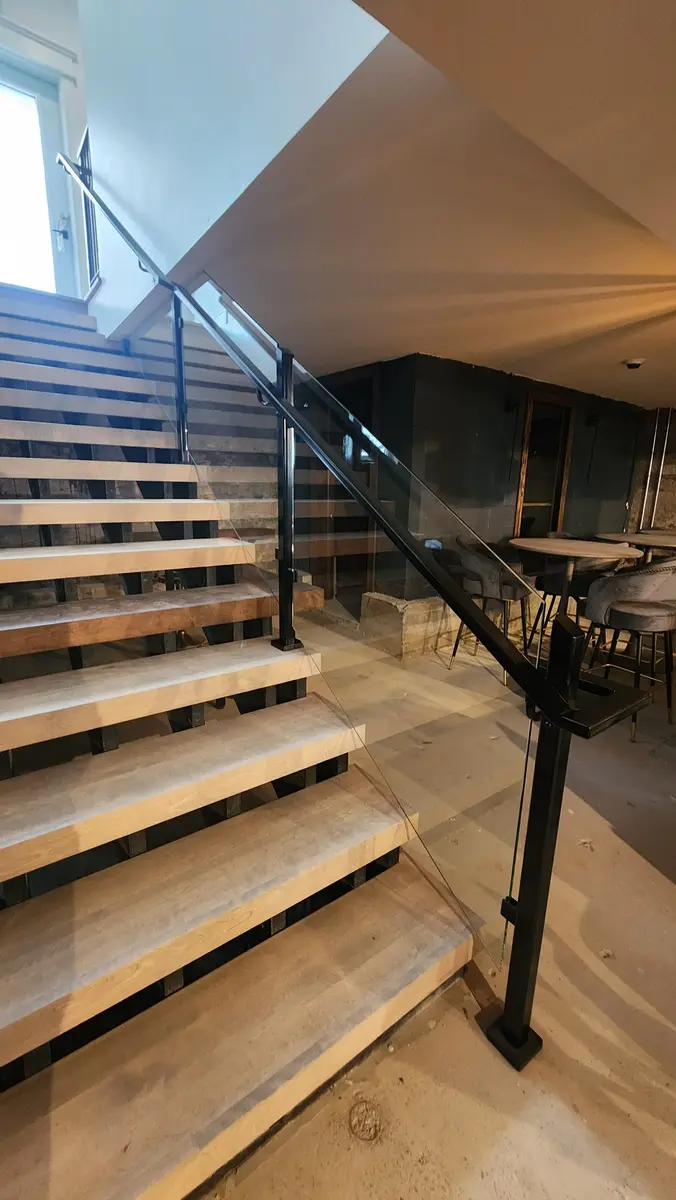 Commercial staircase with glass panels and steel cable railing descending to restaurant bar area