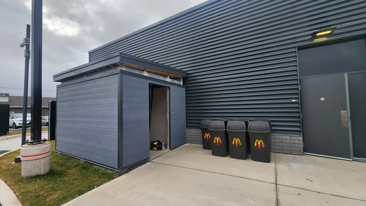 Commercial steel waste enclosure with matching building cladding at drive-thru restaurant