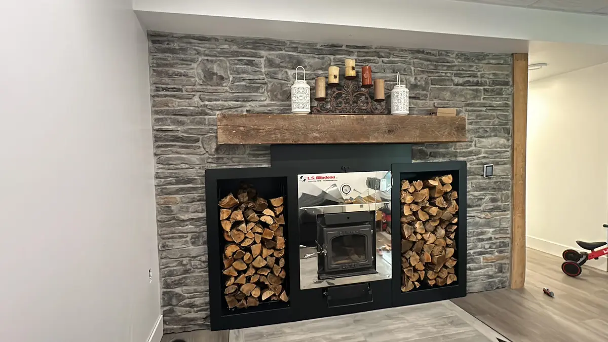 Custom black steel fireplace surround with symmetrical wood storage compartments and rustic beam mantel