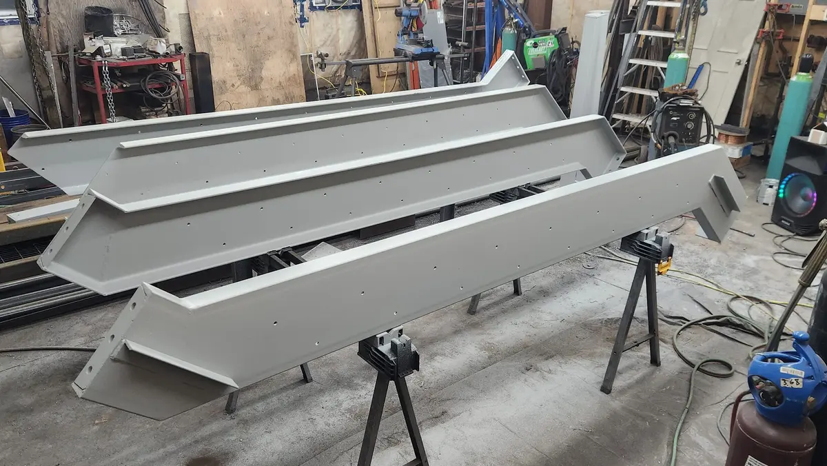 Precision-fabricated painted steel channel brackets on sawhorses in workshop