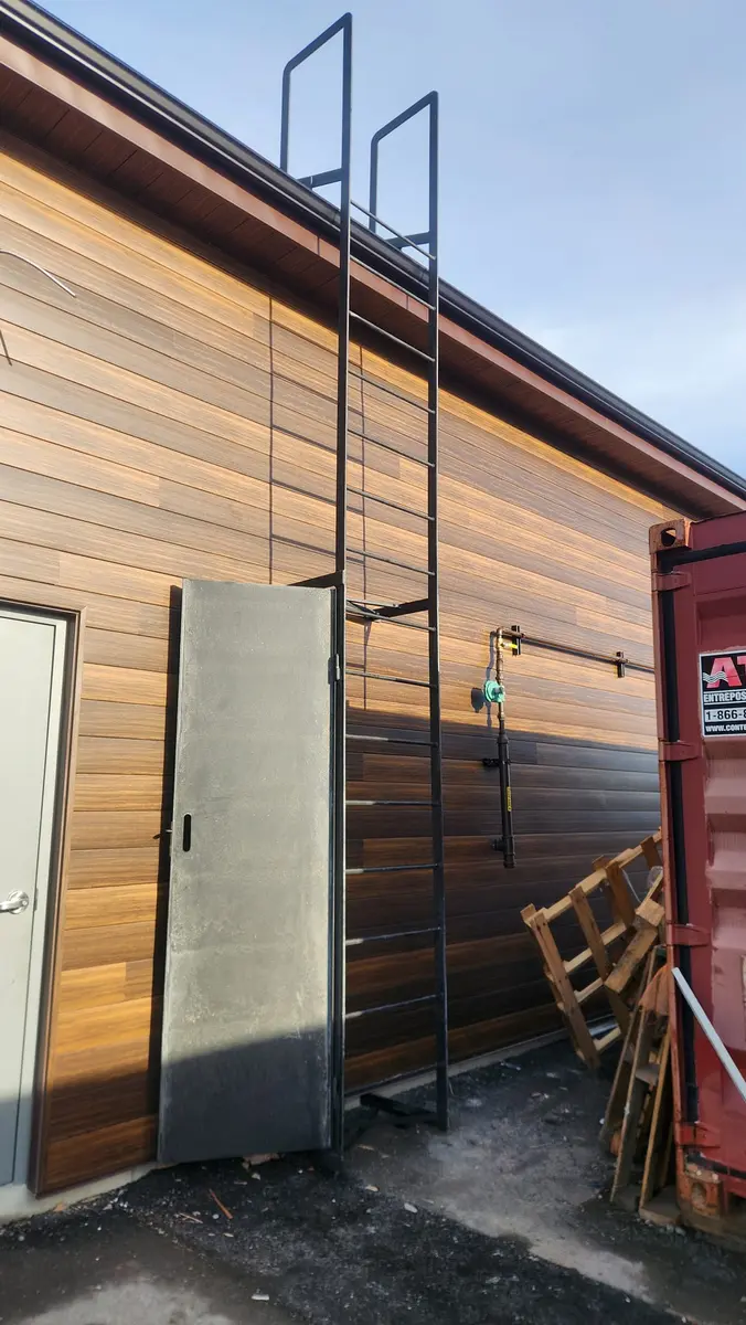 Fixed roof access ladder with safety cage on commercial building exterior