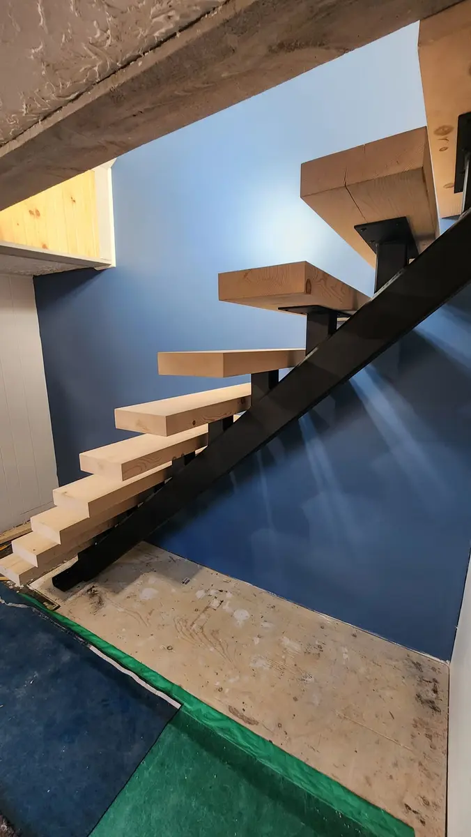 Steel mono-stringer floating stairs with light wood treads descending to basement, blue accent wall