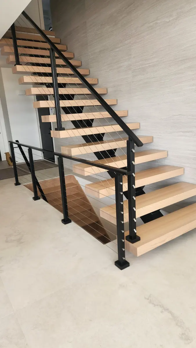 Side view of floating staircase showing cable railing detail and oak treads against stone-look tile wall