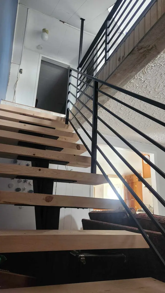 Interior floating stairs with horizontal bar railing, wood treads, and open-concept landing
