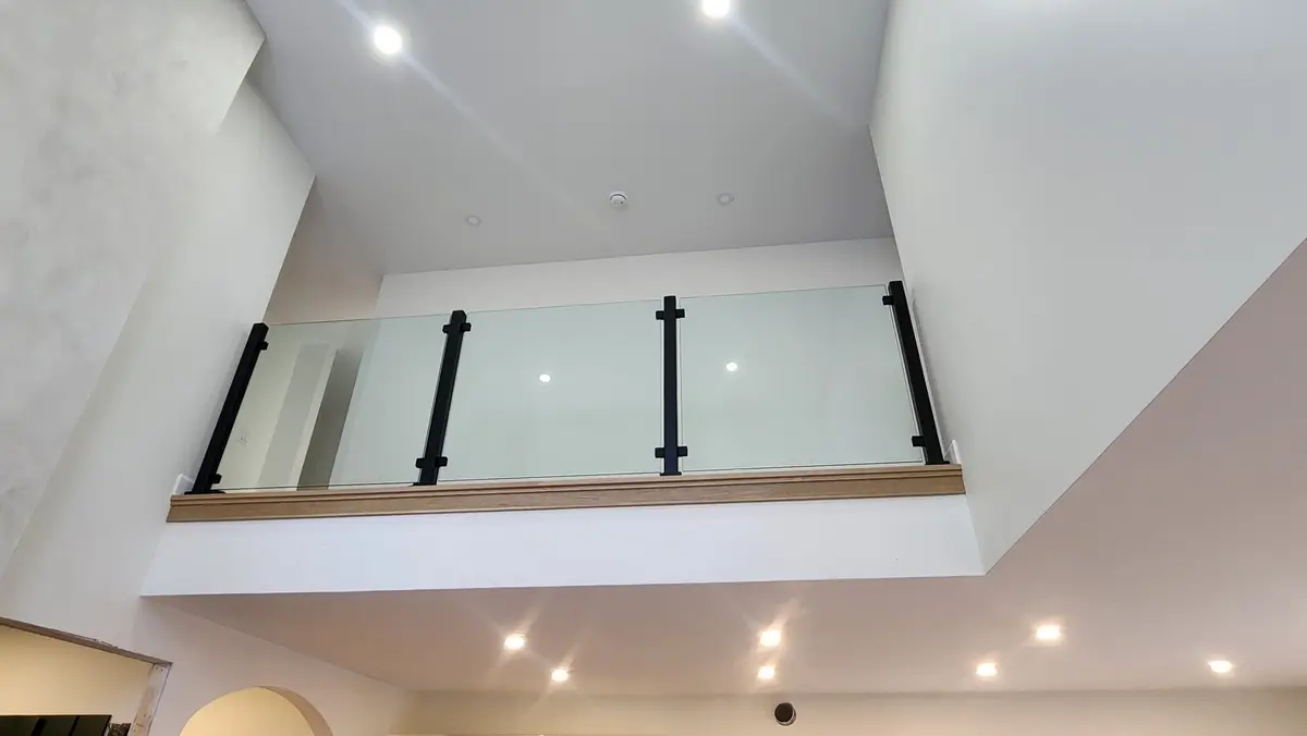 Tempered glass panel loft railing with black steel posts viewed from below in luxury home