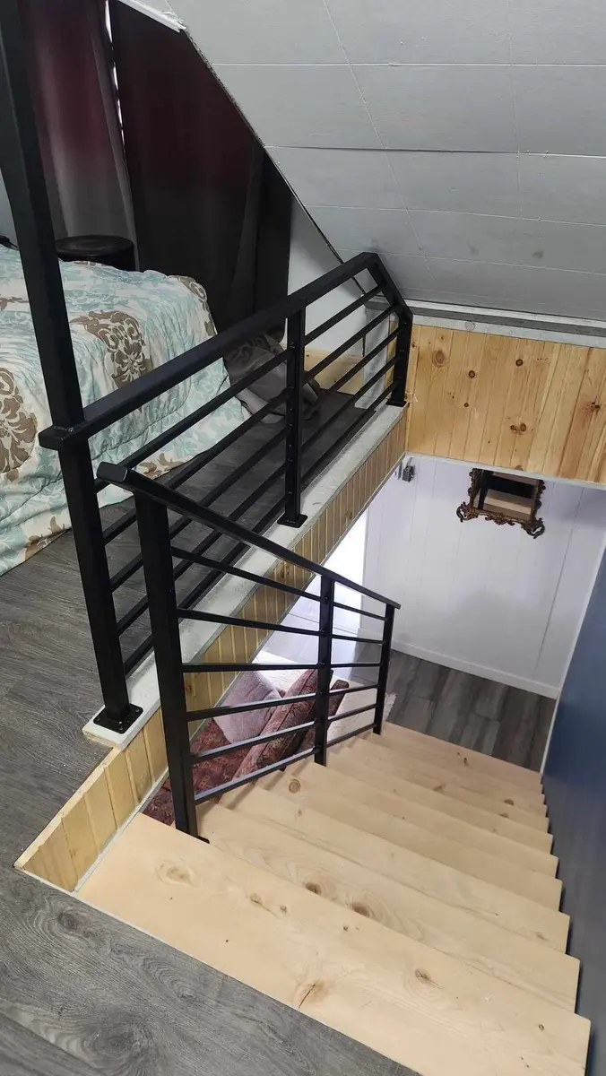 Top-down view of loft stairs with black horizontal bar railing and wood landing