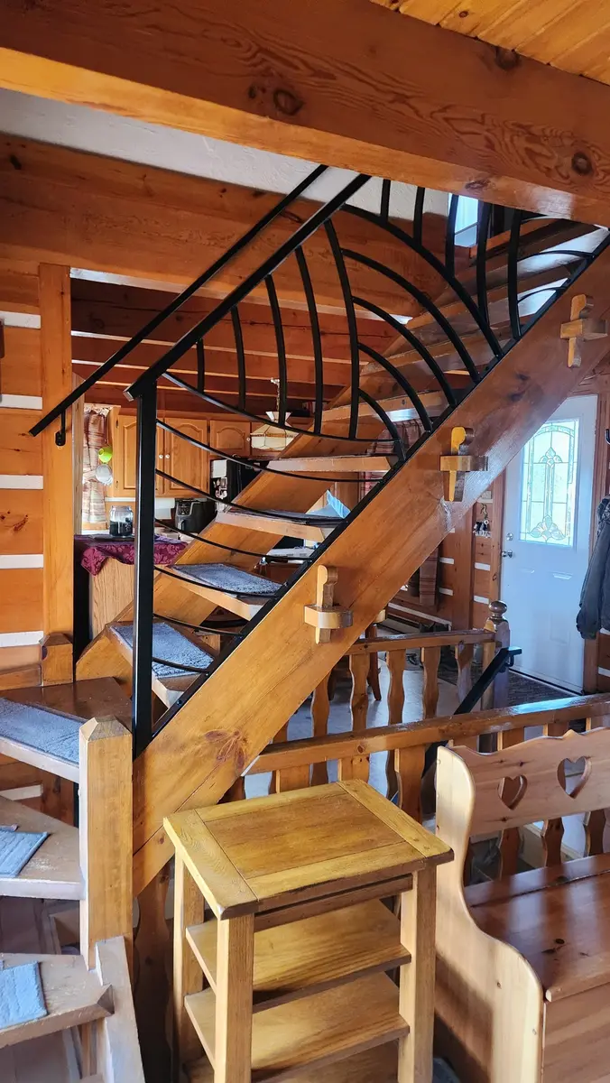 Artistic curved black steel railing in rustic log cabin with open staircase