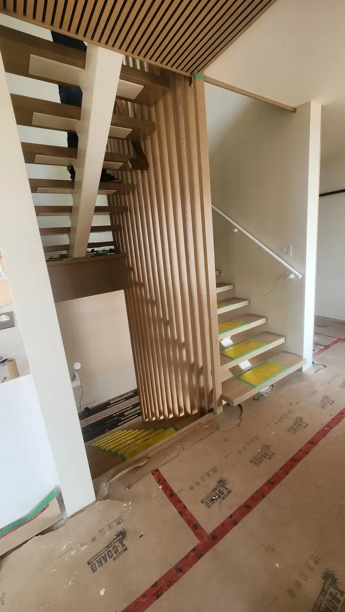 Modern floating staircase with wood slat privacy divider and matching ceiling in new construction