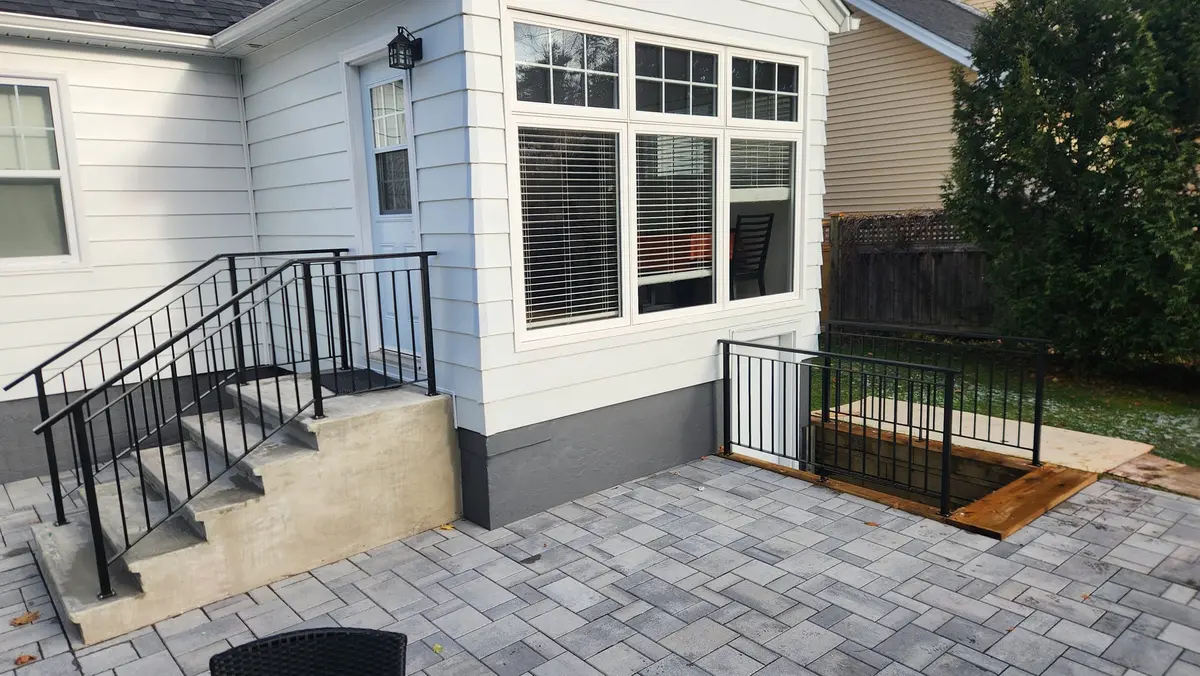 Residential exterior railing on patio with cellar access hatch, black steel with stone pavers