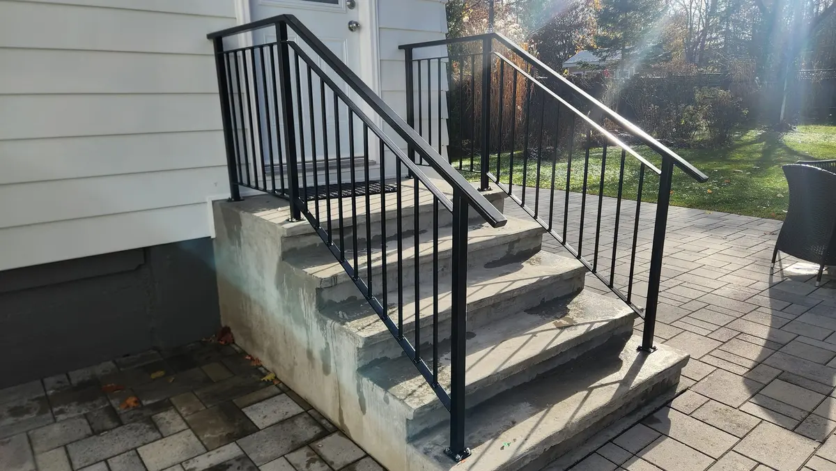 Black steel residential exterior step handrails on concrete steps with paver patio