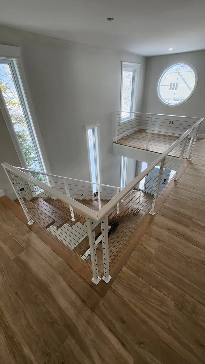 White cable railing system around open loft with porthole window in luxury coastal home